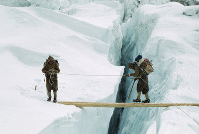 Sherpas in crampons cross a log bridge over a crevasse, Western Cwm