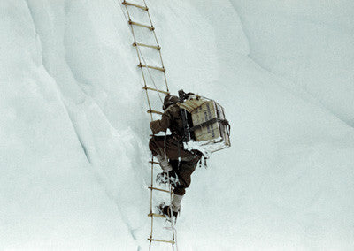 A Sherpa carrying gear on a rope ladder in the icefall